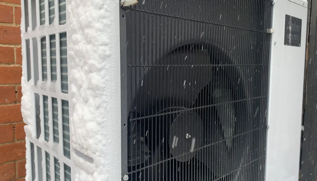 Close-up of a heat pump outdoor unit with frost and snow on the grille.
